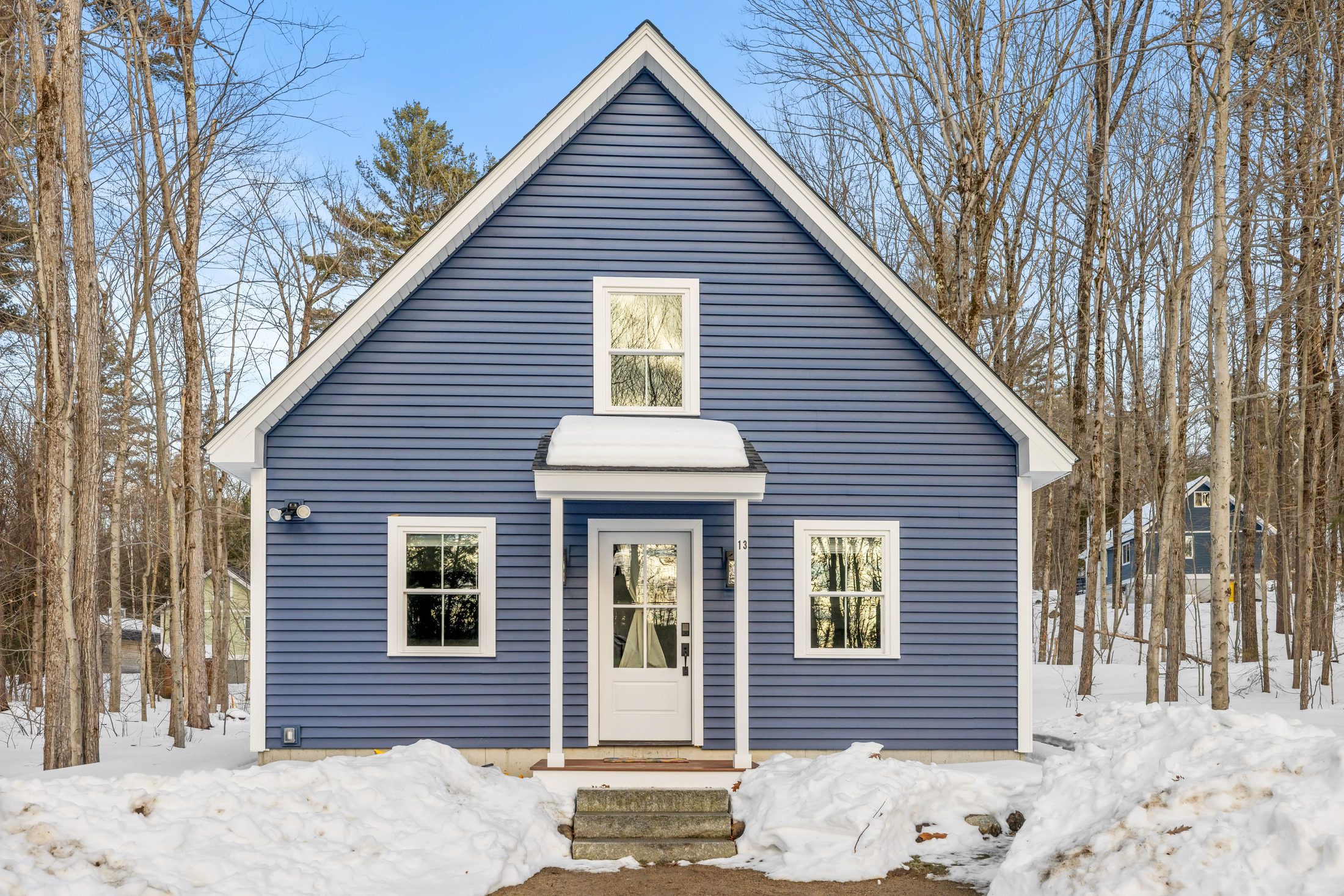 Blue-sided cabin exterior in winter, snow on the ground, surrounded by bare trees