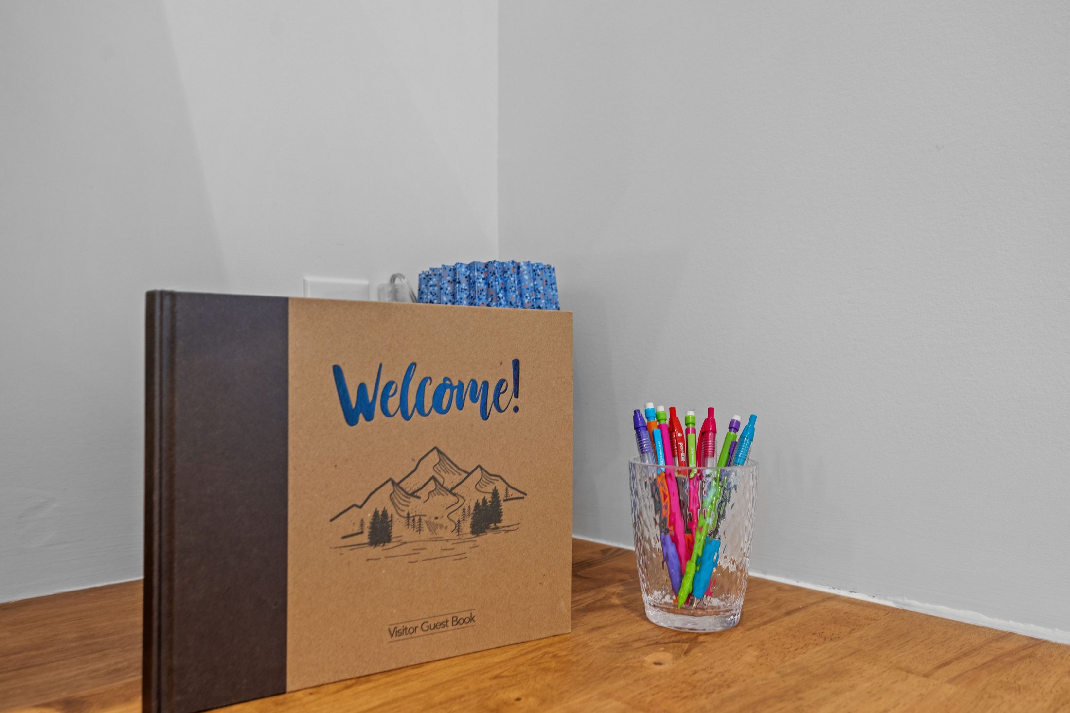 A guest welcome book and a cup of colorful pens on an entry table