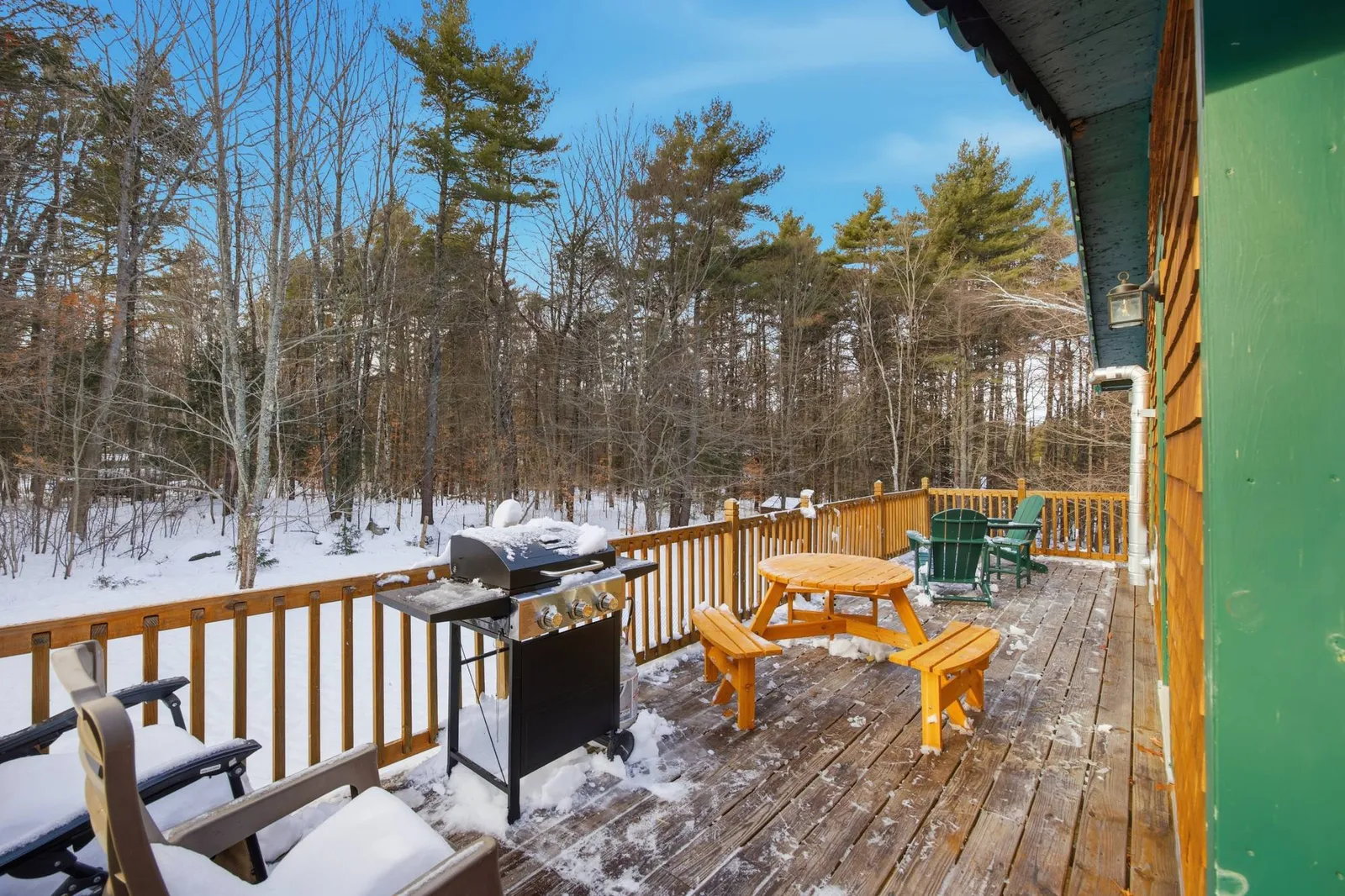 Wraparound deck with a picnic table, grill, and Adirondack chairs, snow on the railings