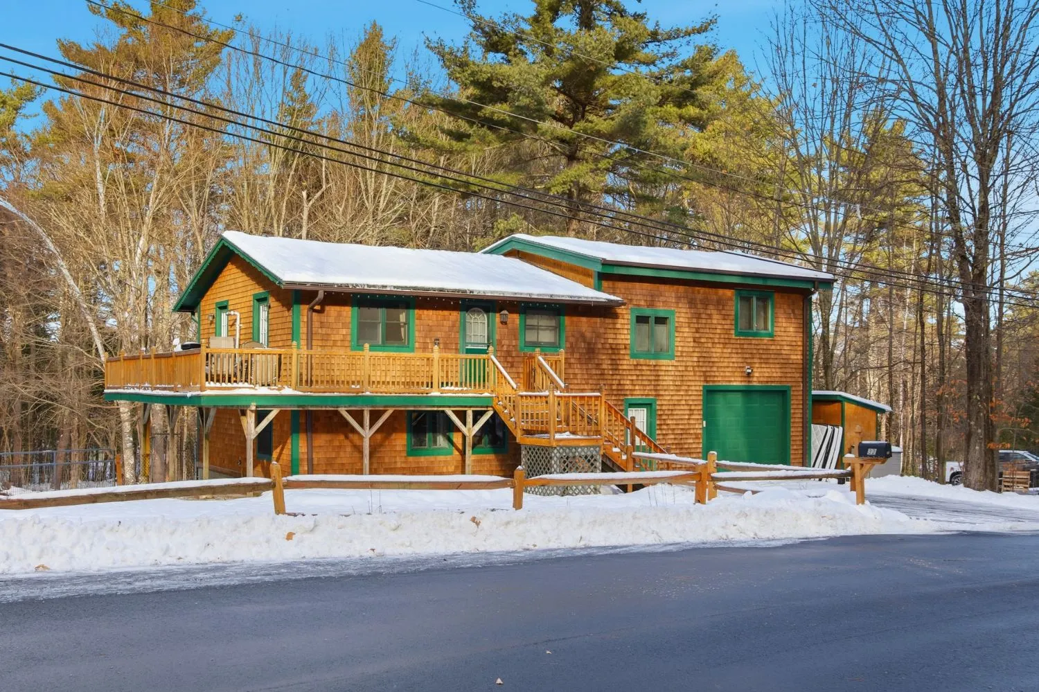 Wood-shingled cabin exterior with green trim, a wraparound deck, and snow on the ground