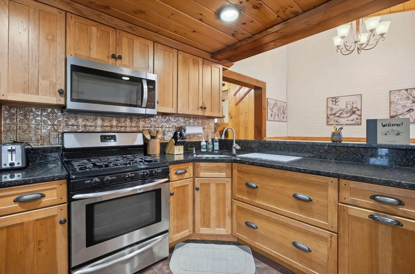 Wood-cabinet kitchen with a gas range, tin backsplash, and dark granite counters